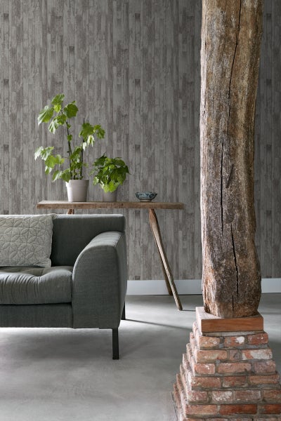 Wohnzimmer mit grauer Couch, Holztisch mit Pflanzen, Holzsäule auf Backsteinsockel und Tapete in Holzoptik