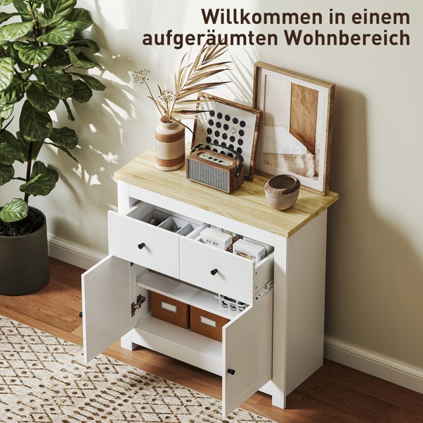 Hell eingerichteter Wohnbereich mit weißem Sideboard mit Holzplatte, das offene Fächer für Besteck und Aufbewahrungsboxen zeigt, und einer Pflanze.