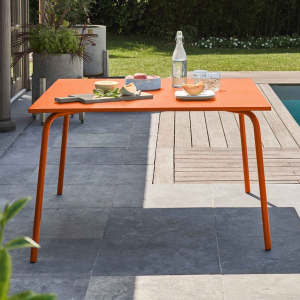Moderner orangefarbener Gartentisch aus Metall auf einer hellen Terrasse mit Steinplatten und Holzdeck neben einem Pool.