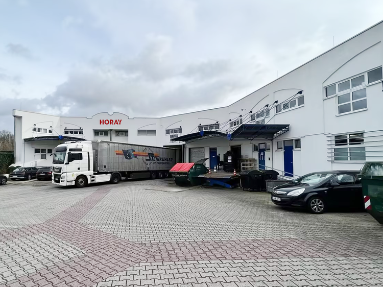Außenansicht eines Lagerhauses mit LKW und mehreren Autos.