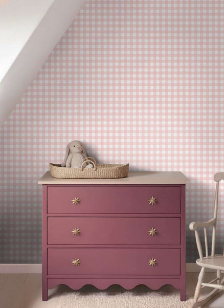 Eine Wand mit karierter Tapete in einem Kinderzimmer, mit einer Kommode, einem Stoffhasen in einem Korb und einem Schaukelstuhl.