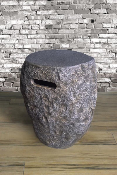 Moderner Hocker in Natursteinoptik mit flacher Sitzfläche und seitlicher Grifföffnung auf einem Holzboden vor einer Backsteinwand.