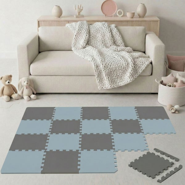 Graue und blaue Puzzlematte aus Schaumstoff in einem hellen, organisierten Kinderzimmer vor einem Sofa mit einer Decke aus Grobstrick.