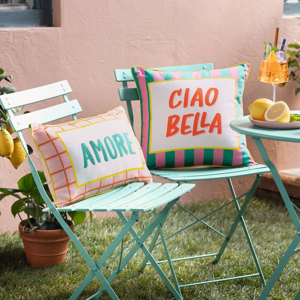 Gartenmöbel-Szene mit zwei Stühlen und einem Tisch mit dekorativen Kissen und Getränken im Freien