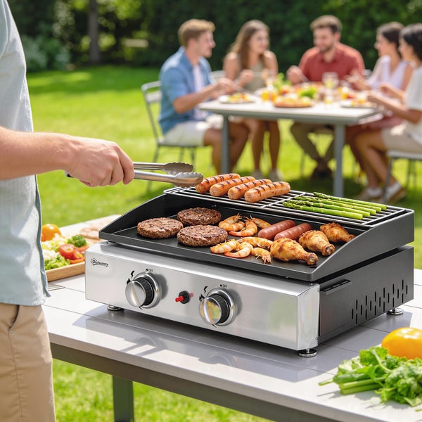 Outsunny Tisch-Gasgrill aus Edelstahl im Garten mit Grillgut wie Fleisch und Spargel, Personen im Hintergrund an einem Tisch.