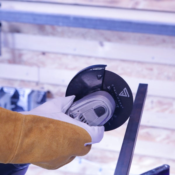 Winkelschleifer von Stahlwerk beim Schneiden eines Metallprofils, geführt von einer Hand in einem ledernen Schutzhandschuh.