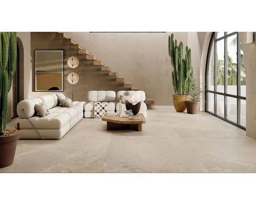 Geräumiges Wohnzimmer mit beigen Fliesen, modernem Sofa, Holztisch, Treppe und großen Kakteen in einer hellen mediterranen Atmosphäre.