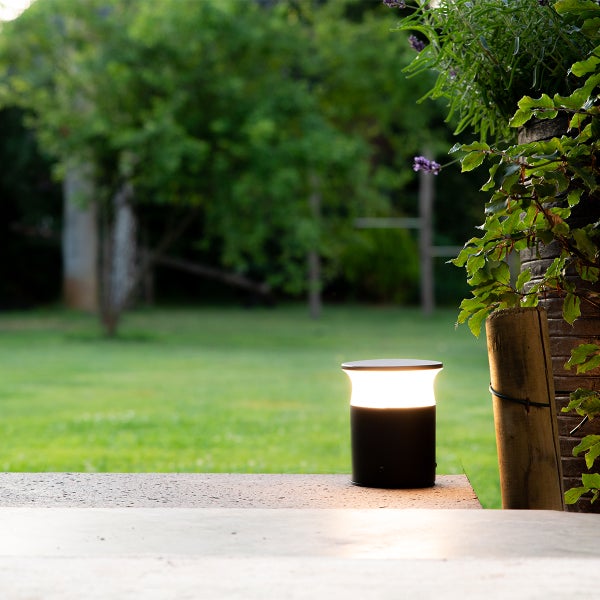 Moderne Wegeleuchte auf einer Terrasse mit Blick in einen grünen Garten.