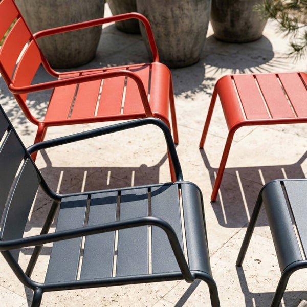 Gartenmöbel-Set aus Metall mit Stühlen und Hockern im Latten-Design auf einer Terrasse mit Steinboden und großen Pflanzkübeln.