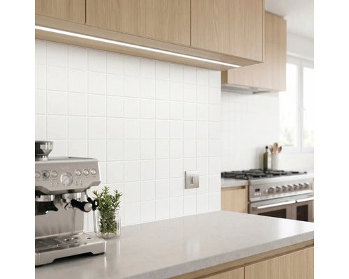 Unterbauleuchte unter Holzschränken beleuchtet eine Küche mit weißem Fliesenspiegel und Espressomaschine.