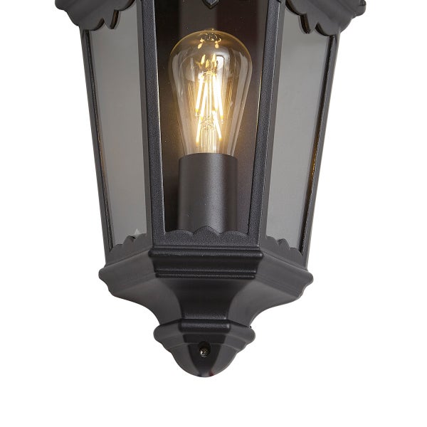Schwarze Außenwandleuchte in Laternenform mit Glaseinsätzen und leuchtendem LED-Filament-Leuchtmittel.