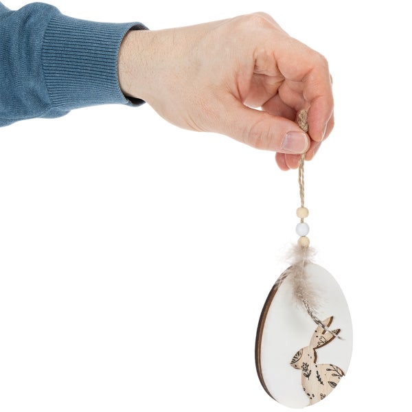 Hand hält einen hölzernen Osteranhänger in Eiform mit einem Hasenmotiv, einer Feder und Holzperlen an einer Schnur.