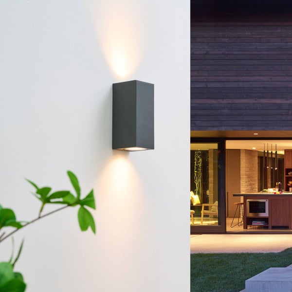 Moderne anthrazitfarbene rechteckige Außenwandleuchte mit Up-and-Down-Lichteffekt an einer weißen Hauswand.