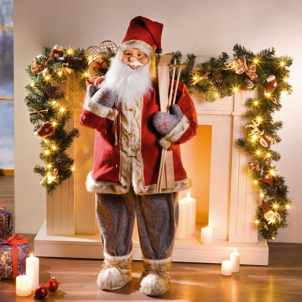 Dekorativer Weihnachtsmann vor einem Kamin mit Weihnachtsschmuck und Kerzen.