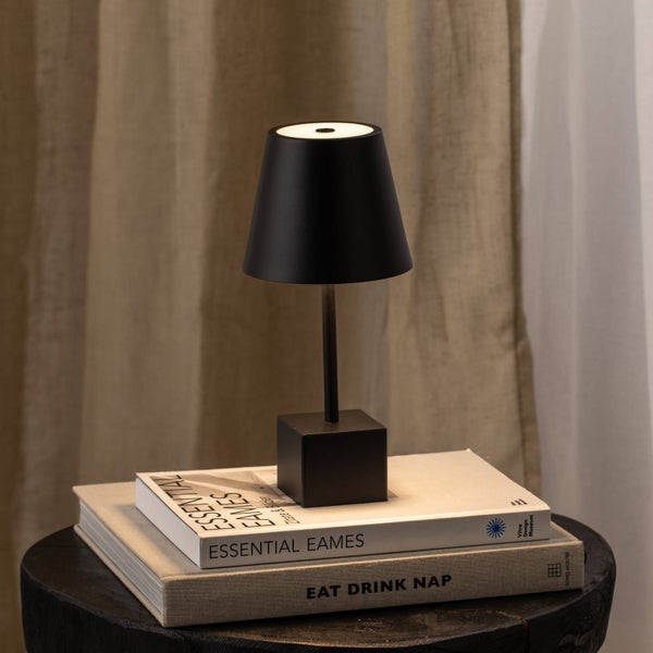 Schwarze Tischleuchte im minimalistischen Design auf Büchern platziert vor einem hellen Vorhang.