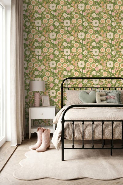 Schlafzimmer mit geblümter Tapete mit Gänseblümchen auf grünem Hintergrund, schwarzem Metallbett und weißem Nachttisch.