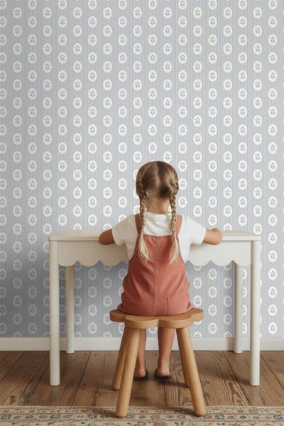 Vliestapete mit Streifenmuster und Blumenmedaillons in einem hellen Kinderzimmer mit Schreibtisch und blumenförmigem Holzschemel.