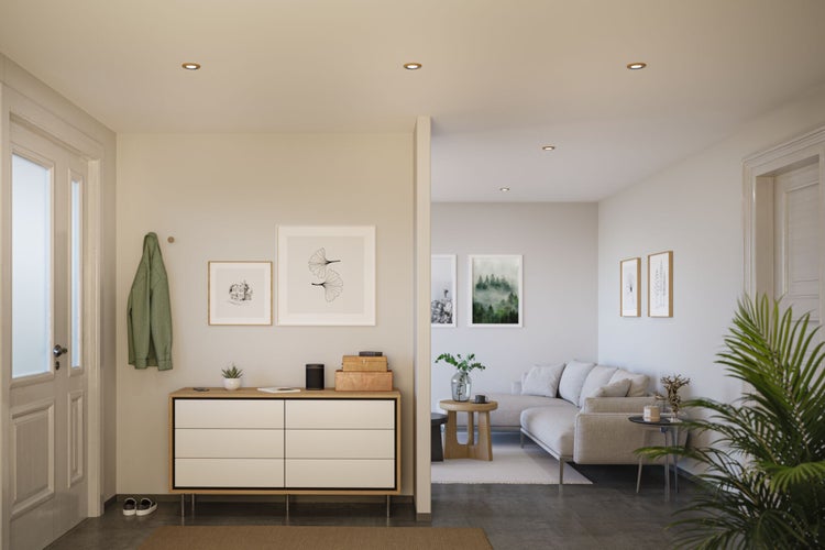 Moderner, heller Flur mit Einbaustrahlern, Holzkommode und angrenzendem Wohnzimmer mit grauem Ecksofa.