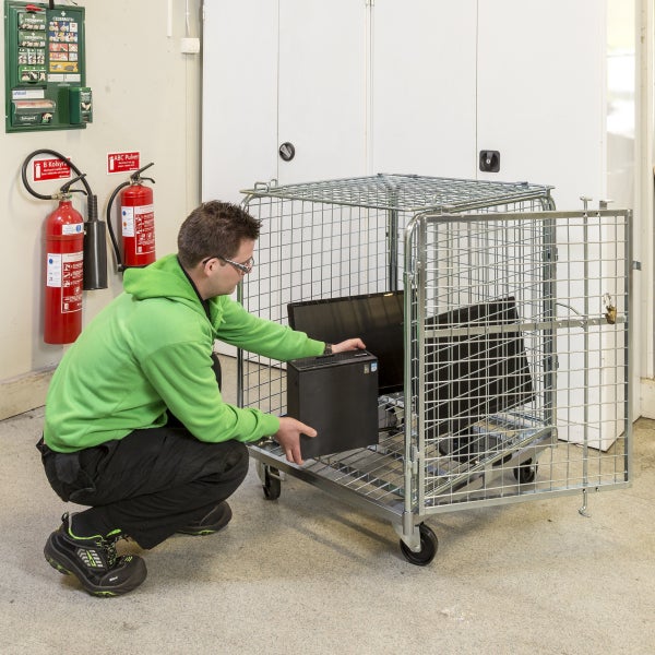 Mann räumt Computer in einen Rollcontainer aus Drahtgitter.