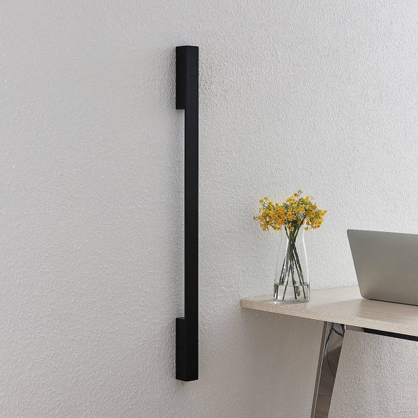 Moderne, schmale, vertikale Wandleuchte in Schwarz an einer Wand in einem hellen Büro mit Schreibtisch, Laptop und Blumen.