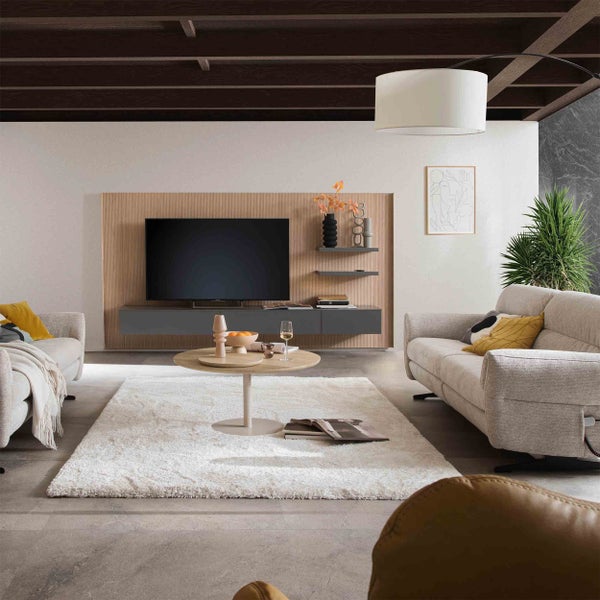 Modernes Wohnzimmer mit Sofas, Teppich, Holz-Couchtisch und Fernseher-Wandpaneel unter Deckenbalken. Helle und geordnete Gestaltung.