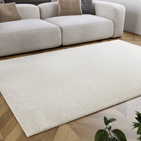 Rechteckiger heller Teppich in einem hellen Wohnzimmer vor einem modernen Sofa auf einem Parkettboden.