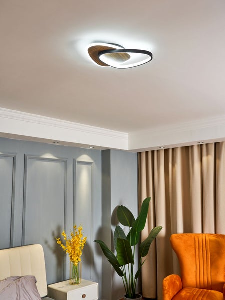 Moderne LED-Deckenleuchte in Schlaufenform mit Holzoptik und schwarzem Rahmen an einer Decke im Wohnzimmer.