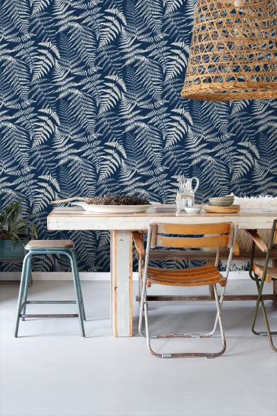 Szene mit Tisch und Stühlen vor einer Wand mit Farnmuster-Tapete.