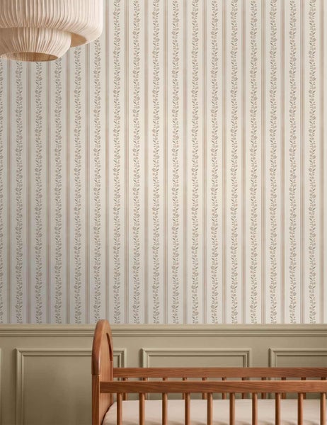 Vliestapete mit feinen vertikalen Streifen und Blumenranken in einem hellen Kinderzimmer mit einem Kinderbett aus Holz.