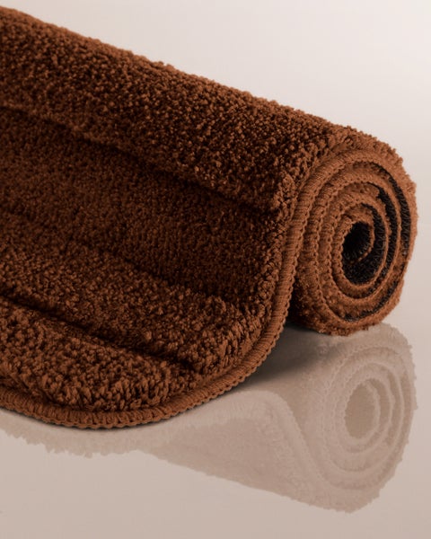 Aufgerollte braune Badematte mit weicher Hochflor-Struktur.