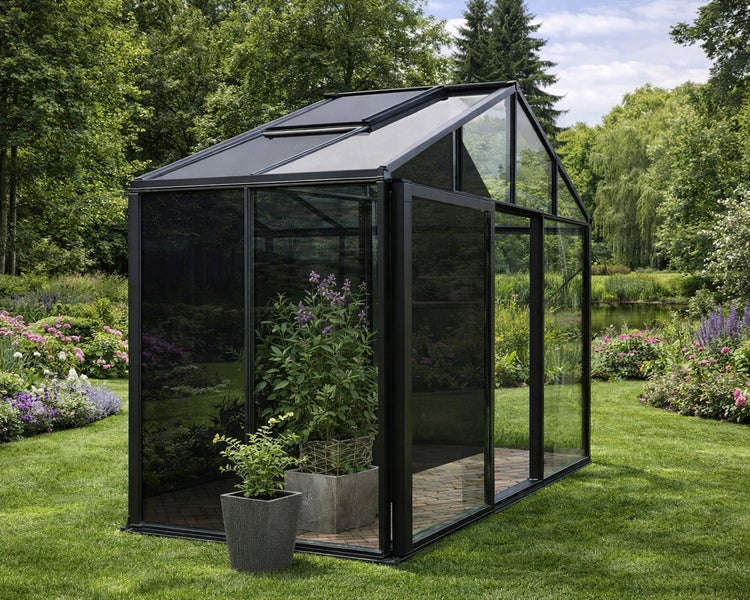 Modernes schwarzes Gewächshaus mit Glaswänden und Dachfenster in einem Garten mit Blumen und Pflanzen in Töpfen.