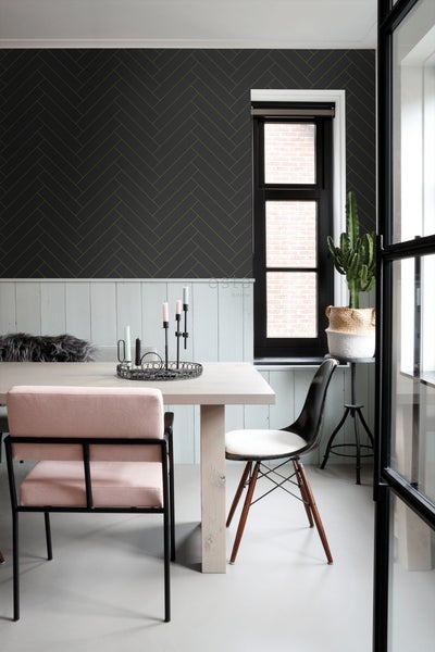 Heller Esstisch mit Stühlen, dekorativen Kerzen und einer Kaktuspflanze vor einer Wand mit Fischgrätmuster-Tapete.