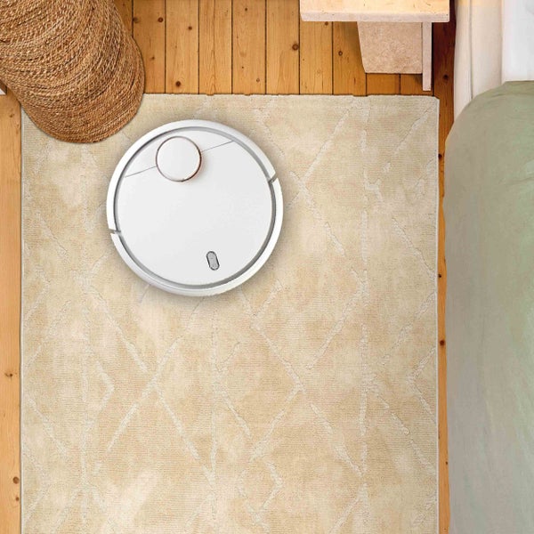 Ansicht von oben: Saugroboter auf einem Teppich, neben einem Korb und einem Bett.