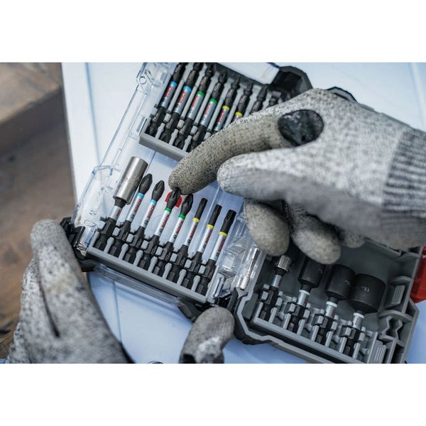 Ein Satz Schrauberbits und Steckschlüsseleinsätze in einem durchsichtigen Kunststoffkoffer, gehalten von zwei behandschuhten Händen.