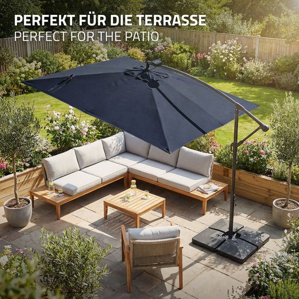 Großer Ampelschirm über einer Ecklounge aus Holz mit Polstern und einem Gartentisch auf einer Terrasse in einem blühenden Garten.