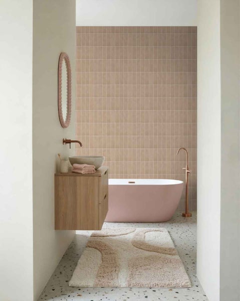Modernes Badezimmer mit freistehender Wanne, Waschtisch in Holzoptik, rundem Spiegel und gefliester Wand in einem hellen, aufgeräumten Raum.