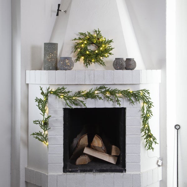 Dekorierter Kamin mit Tannengirlande, Adventskranz und Windlichtern für eine weihnachtliche Atmosphäre.