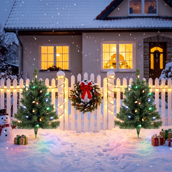 Familie im verschneiten Garten mit zwei beleuchteten künstlichen Weihnachtsbäumen, die keine Pflege benötigen und schwer entflammbar sind.