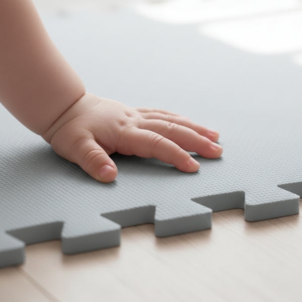 Babyhand auf einer grauen Schaumstoff-Puzzlematte mit strukturierter Oberfläche und verzahnten Rändern.
