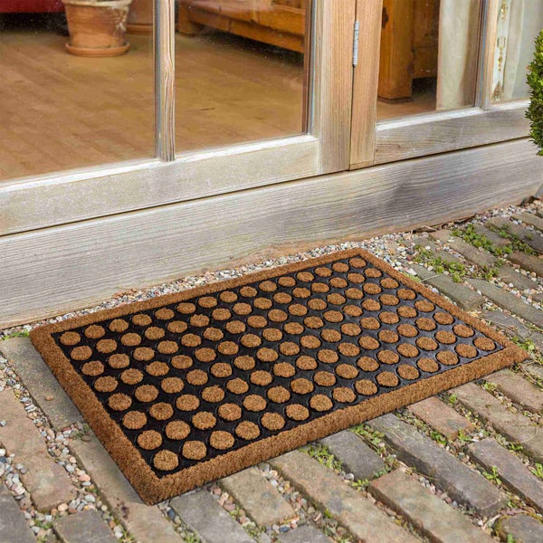 Fußmatte aus Kokosfaser mit Noppenmuster vor einer Holztür