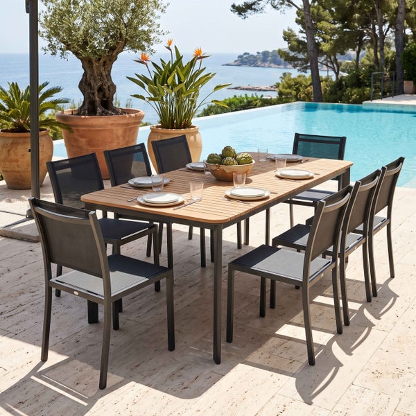 Modernes Gartenmöbel-Set mit rechteckigem Holztisch und acht Stühlen mit dunklem Metallgestell und Netzgewebe auf einer hellen Steinterrasse am Pool.
