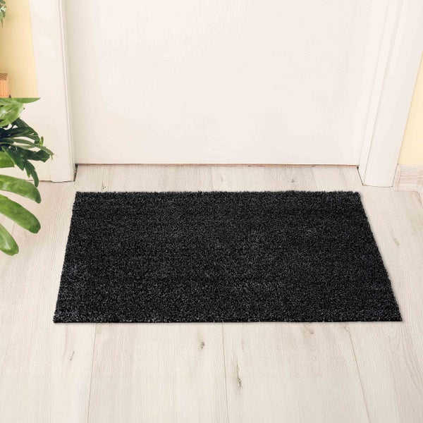 Rechteckige Hochflor-Fußmatte in Schwarz vor einer weißen Tür auf hellem Holzboden.