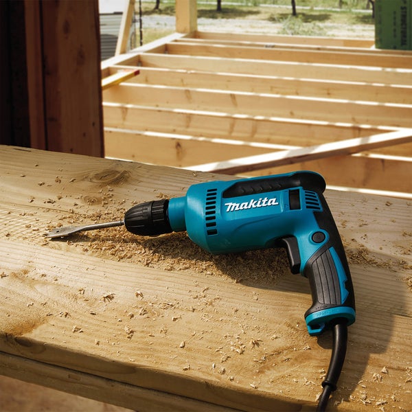 Makita Bohrmaschine mit Flachfräsbohrer auf einem Holzbalken mit Holzspänen auf einer Baustelle.