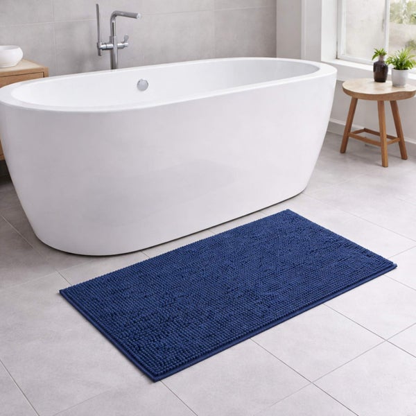 Blaue Badematte in Chenille-Optik vor einer weißen, freistehenden Badewanne in einem hellen, modern gestalteten Badezimmer.