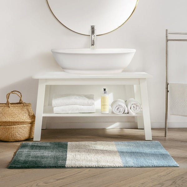 Badezimmer mit Waschtisch, Spiegel, Handtüchern, Wäschekorb und Badteppich