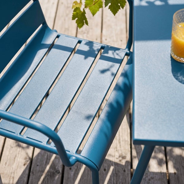 Blauer Gartenstuhl aus Metall und passender Metalltisch auf einer Terrasse aus Holzlatten.