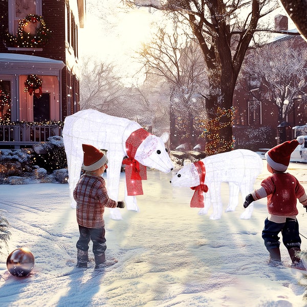 Zwei beleuchtete Eisbären-Weihnachtsfiguren mit roten Schleifen in einer verschneiten Außenanlage mit Haus und Kindern.