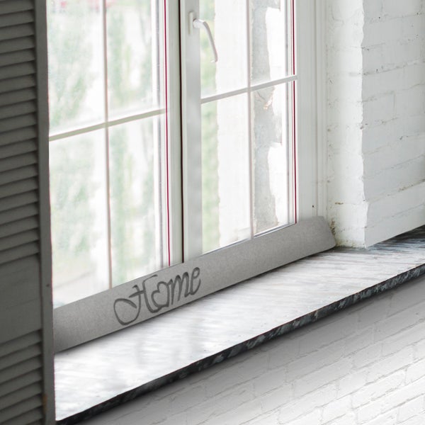 Zugluftstopper mit dem Schriftzug Home vor einem Fenster