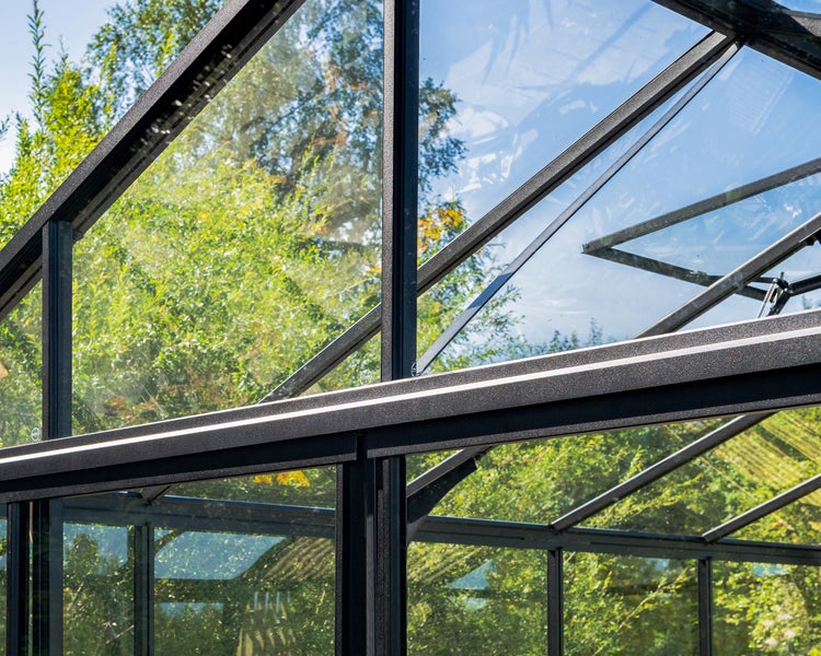 Gewächshaus mit schwarzem Aluminiumrahmen und Glaspaneelen, Detailansicht der Dach- und Seitenkonstruktion.