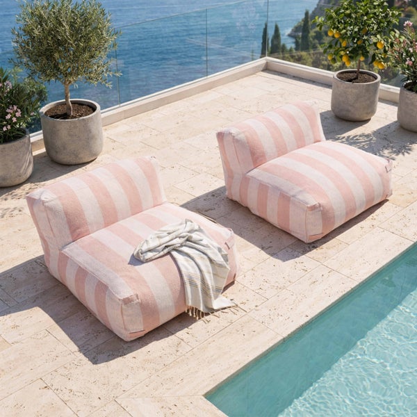 Zwei gestreifte Outdoor Sitzsäcke auf einer Steinterrasse neben einem Pool mit Blick auf das Meer und mediterranen Pflanzen.